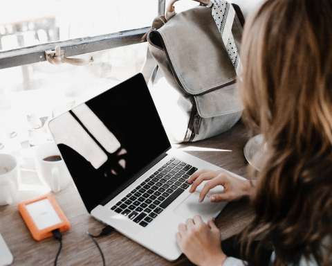 girl wearing grey long-sleeved shirt using MacBook Pro on brown wooden table