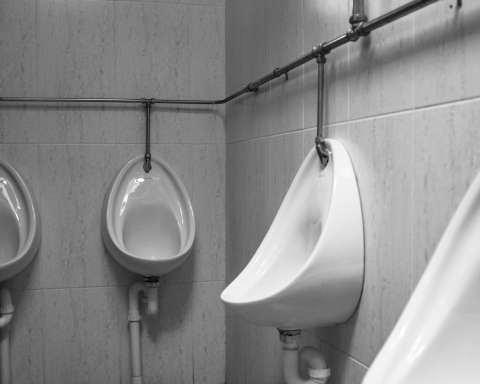 grayscale photography of four white ceramic urinal sinks